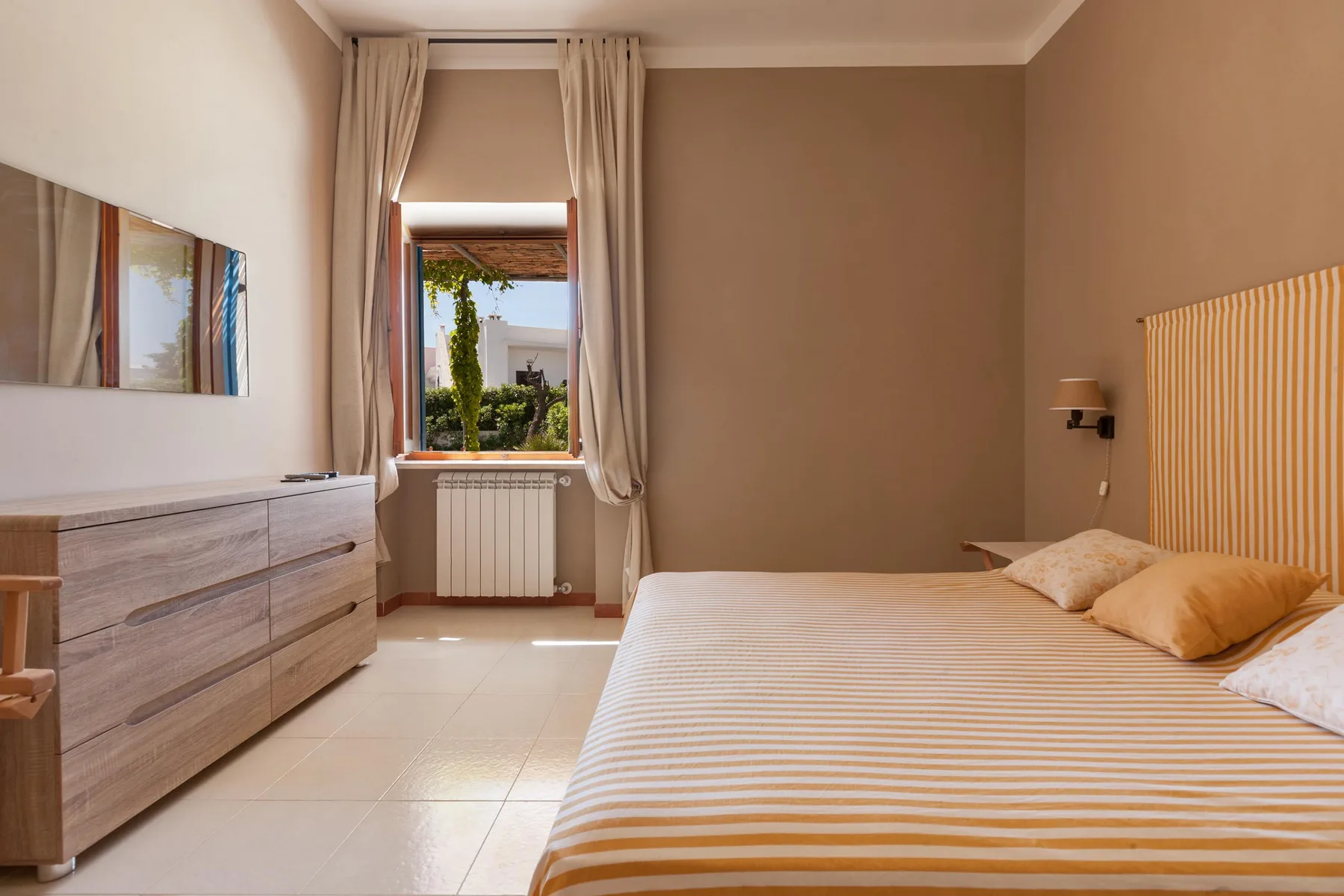 Un dormitorio con una colcha a rayas y una ventana enmarcada por cortinas.