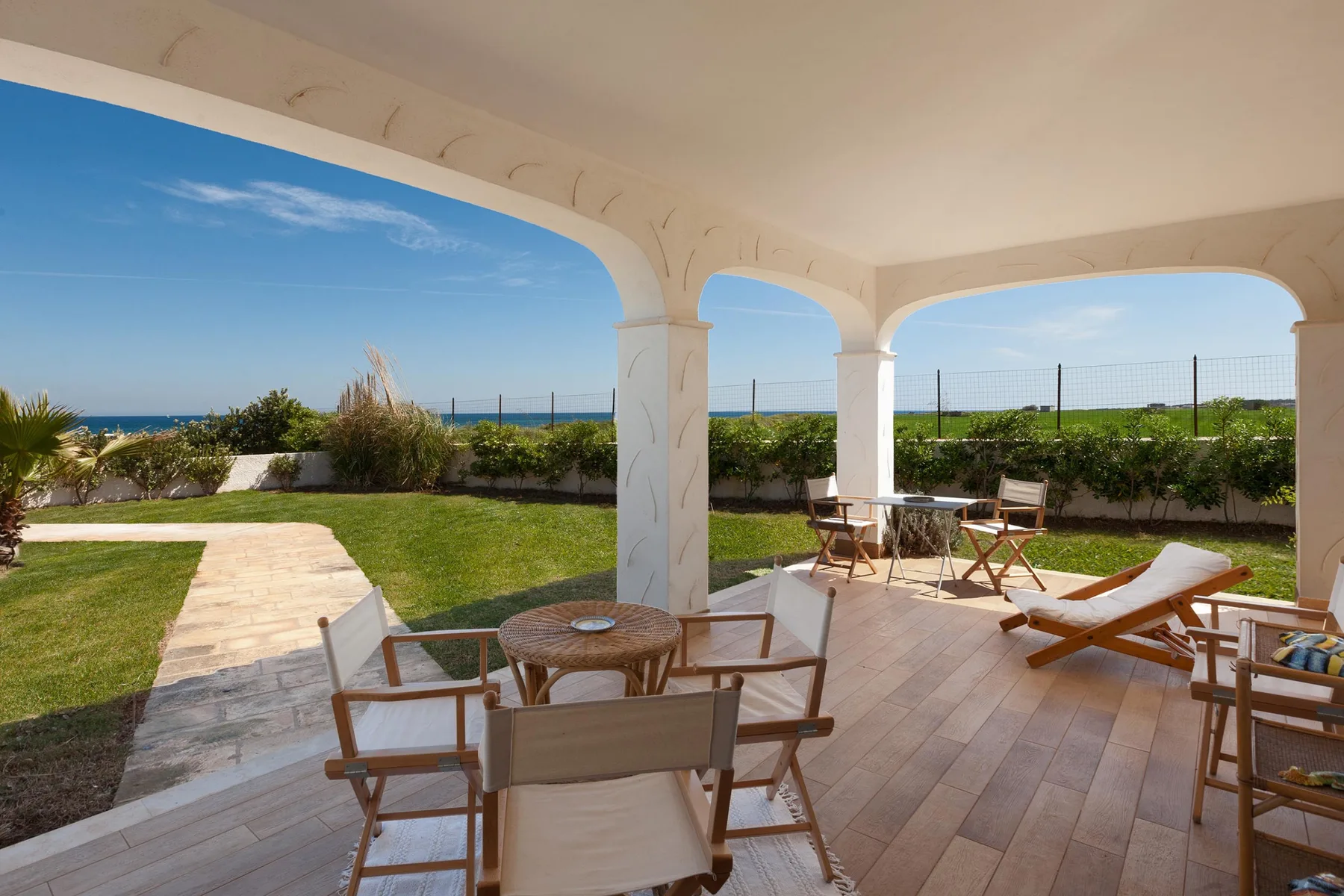 A covered patio with seating overlooks a garden and the sea.
