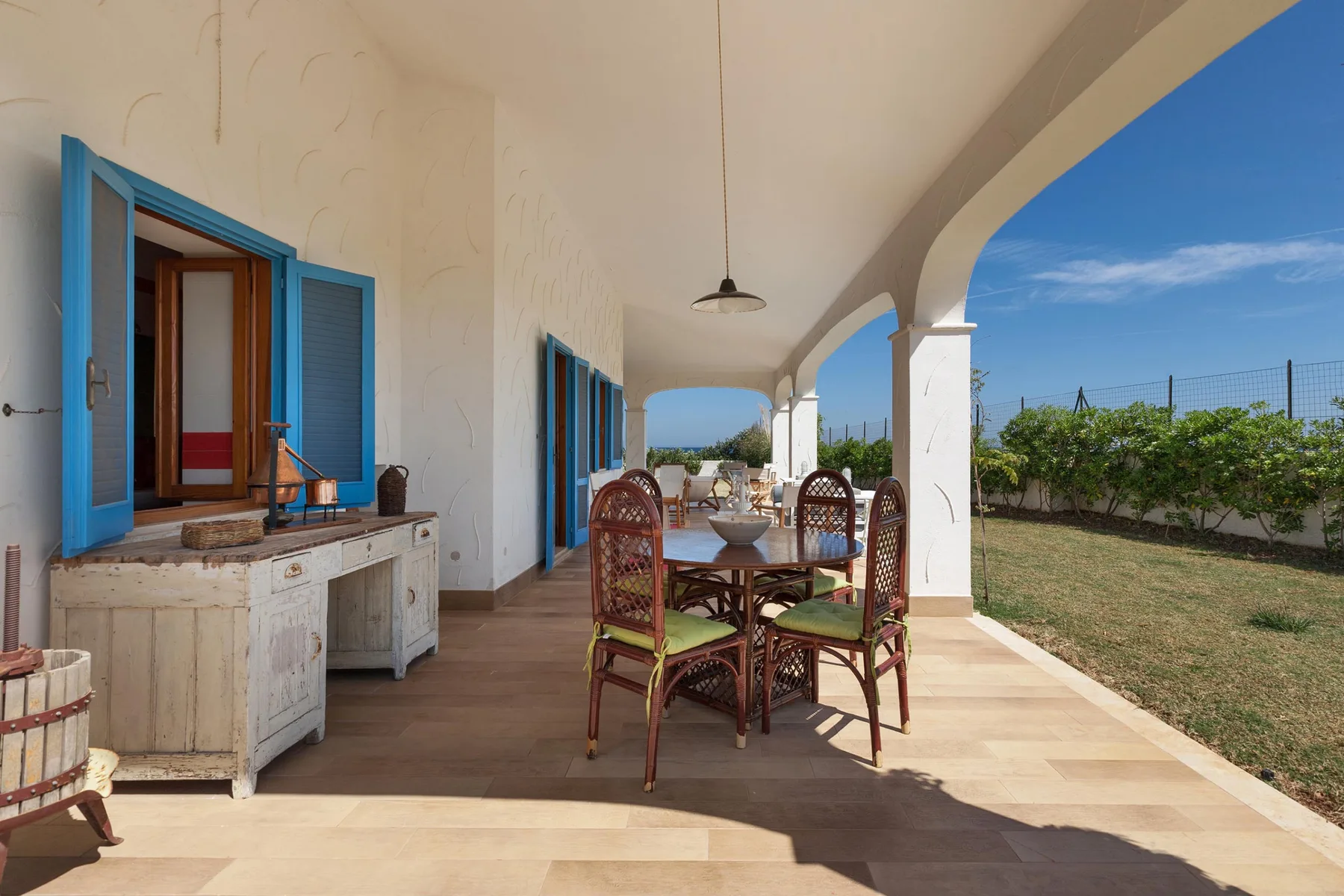 Una zona de comedor exterior cubierta con una mesa y asientos junto a contraventanas azules abiertas.