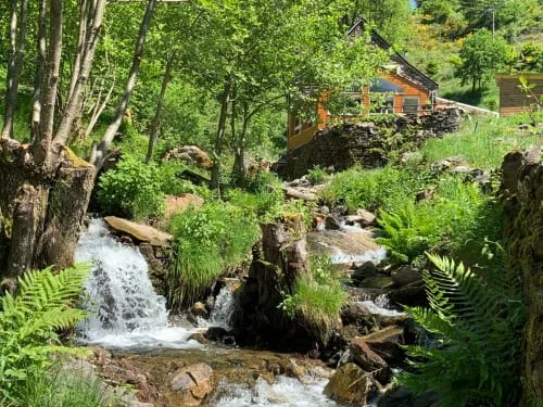 Stone guesthouse beside a stream and wooded hills.