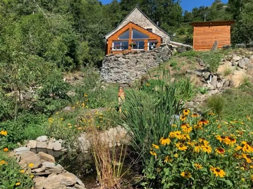 Stone guesthouse surrounded by flowers.