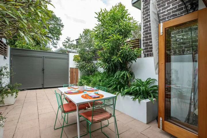 Un patio al aire libre con una mesa, sillas y vegetación alrededor.