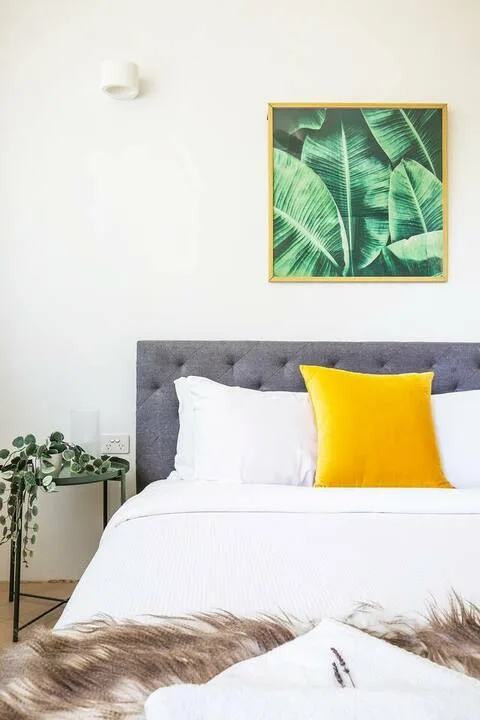 Un dormitorio luminoso con una cama bien tendida y arte botánico en la pared.