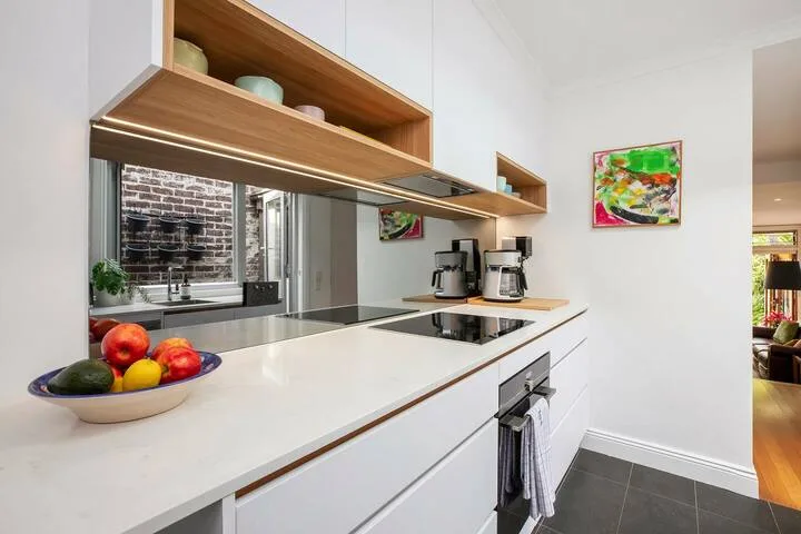 Una cocina moderna con una larga encimera blanca, una placa de cocina y un frutero.