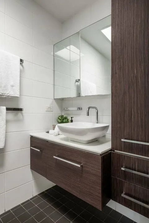 Un baño moderno con lavabo blanco, armario con espejo y suelo de baldosas oscuras.