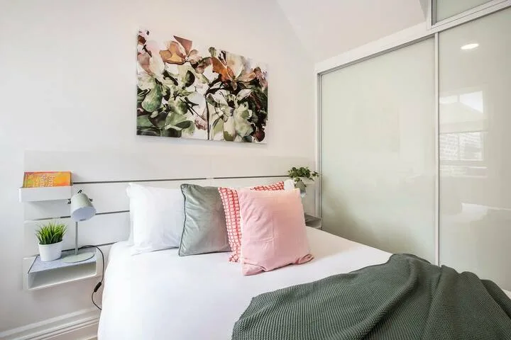 Un dormitorio con una cama tendida, almohadas de colores y arte floral en la pared.