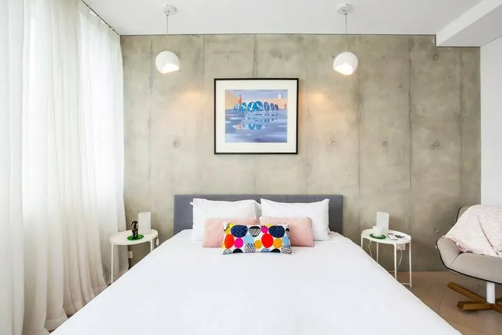 Un dormitorio luminoso con una cama bien tendida y una lámina enmarcada en la pared.