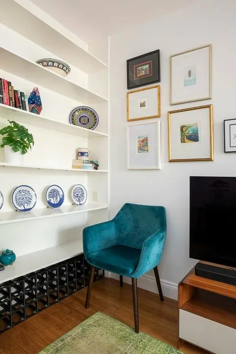 Un sillón tapizado de color verde azulado está junto a estantes empotrados y cuadros enmarcados.