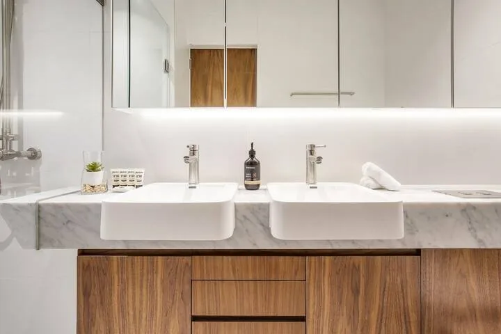 Un tocador de baño moderno con dos lavabos, encimera de mármol y gabinetes de madera.