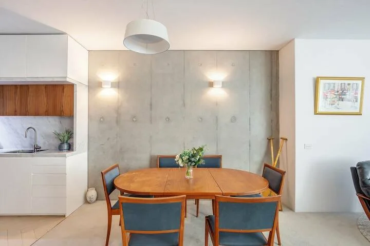 Un comedor con una mesa de madera, sillas y un jarrón con flores.