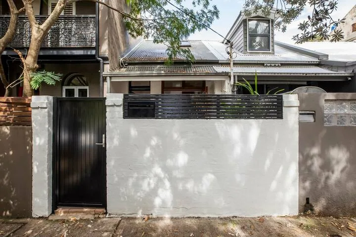 Exterior de una casa tras un muro blanco y una puerta negra.