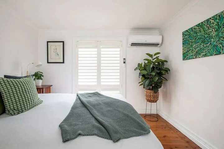 Un dormitorio luminoso con una cama, una ventana con postigos y una planta en maceta.