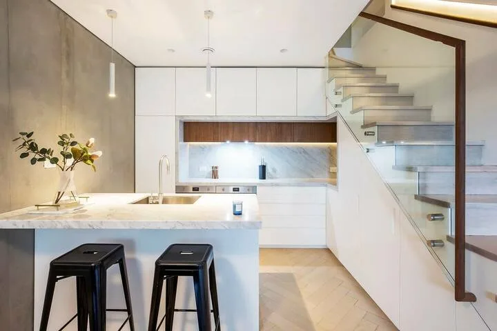 Una cocina moderna con una isla de mármol y una escalera al fondo.