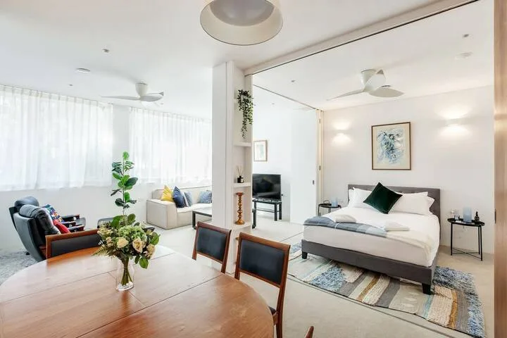 Un dormitorio luminoso con una cama, una zona de estar y una mesa de comedor de madera.