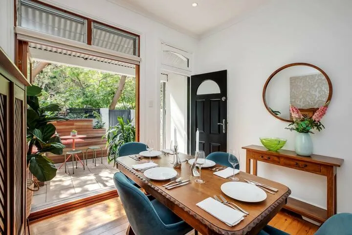 Comedor con una mesa de madera preparada junto a puertas abiertas a un patio frondoso.
