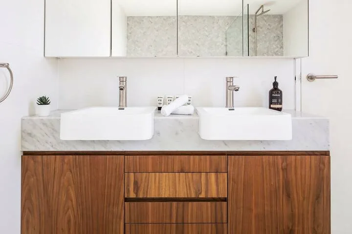 Un mueble de baño con dos lavabos, un espejo amplio y armarios de madera.