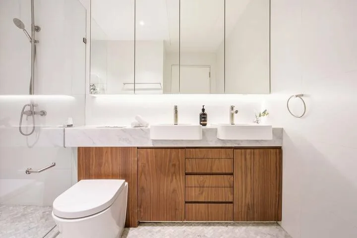 Un baño luminoso con lavabo doble y muebles de madera.