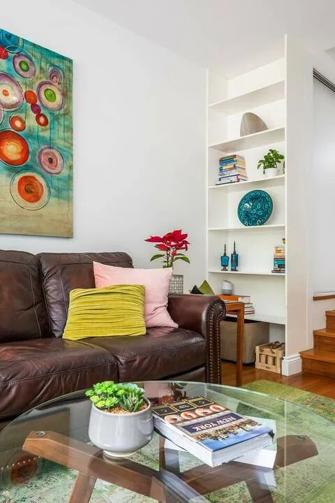 Una sala de estar con asientos oscuros, una mesa de centro de vidrio y estanterías empotradas.