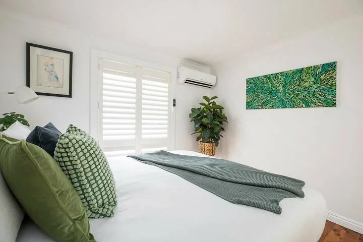 Un dormitorio luminoso con una cama, cojines verdes y una planta en maceta.