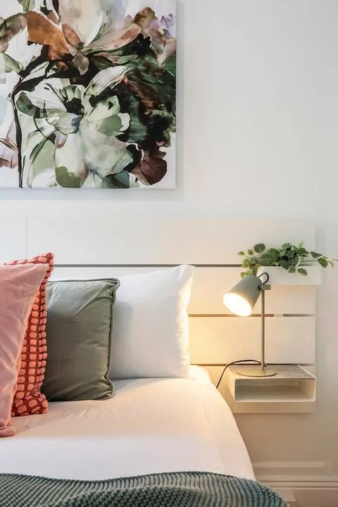 Un dormitorio con una cama tendida, cojines de colores y arte floral en la pared.