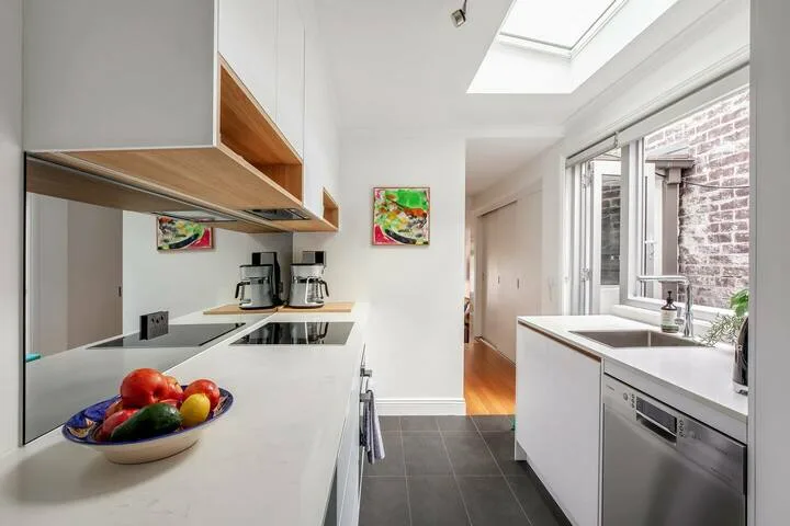 Una cocina luminosa con encimeras blancas, una claraboya y grandes ventanas.