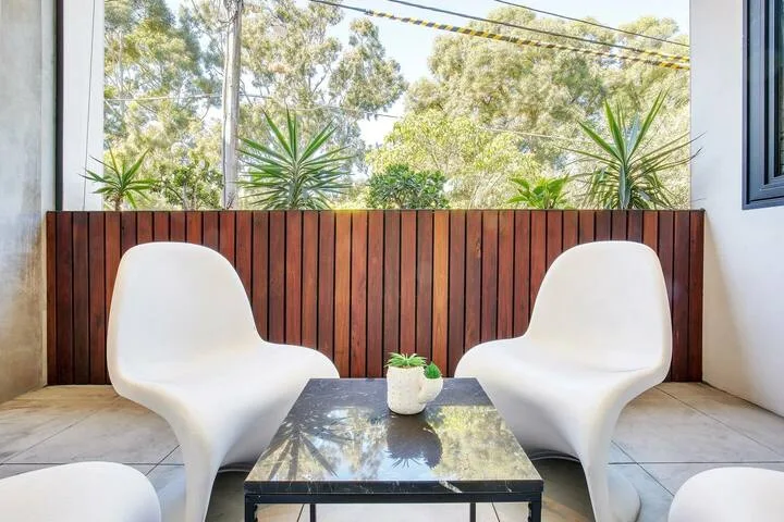 Una zona de estar luminosa tiene asientos blancos junto a una mesa baja y grandes ventanas.