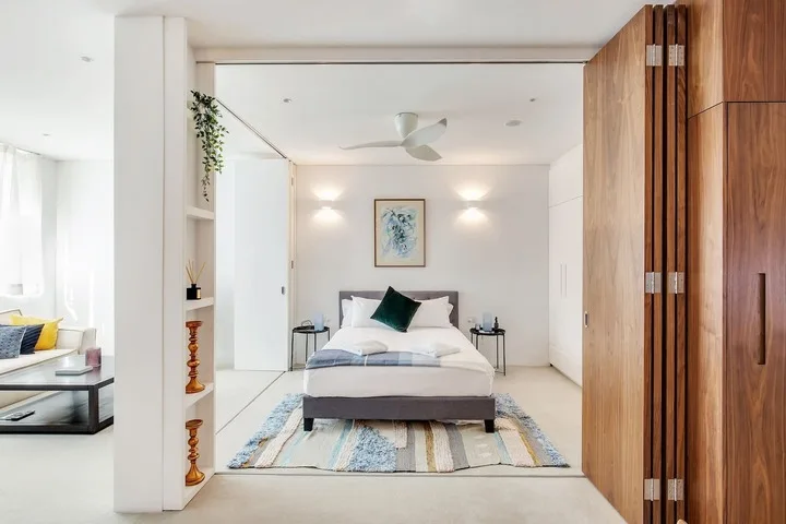 Un dormitorio luminoso con una cama, mesitas de noche y un ventilador de techo.