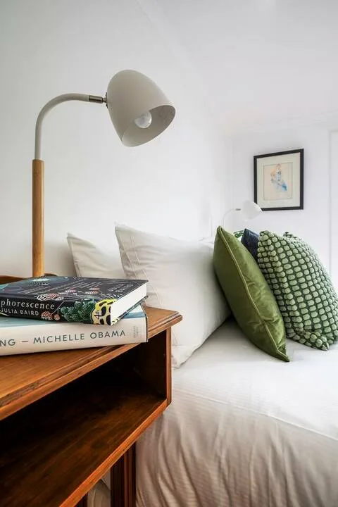 Un dormitorio luminoso con ropa de cama blanca, cojines verdes y una lámpara.