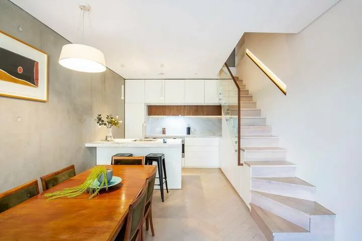 Un comedor luminoso con cocina, mesa de madera y escalera.