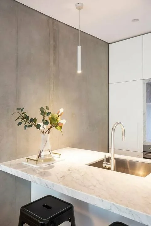Una cocina moderna con una isla de piedra clara, un grifo alto y un jarrón con flores.