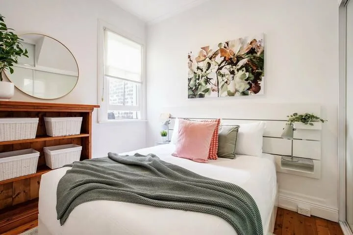 Un dormitorio luminoso con una cama, arte floral en la pared y estantes de madera.
