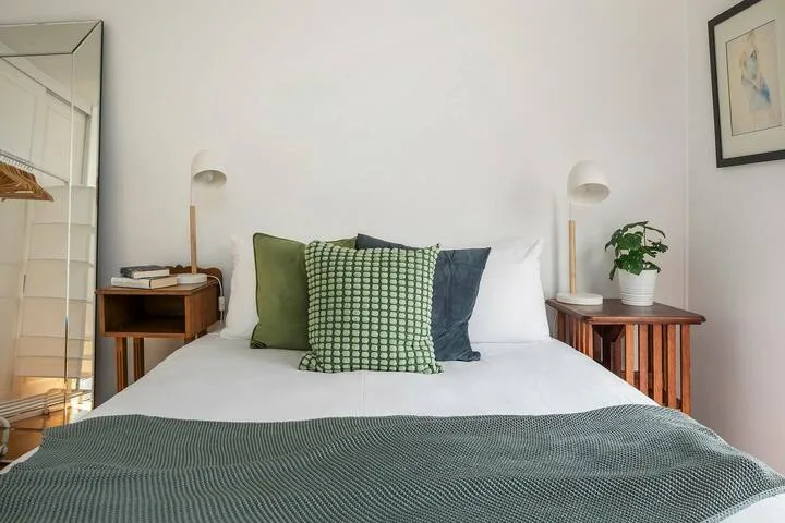 Una cama bien tendida con cojines verdes y blancos está entre dos mesitas de noche.