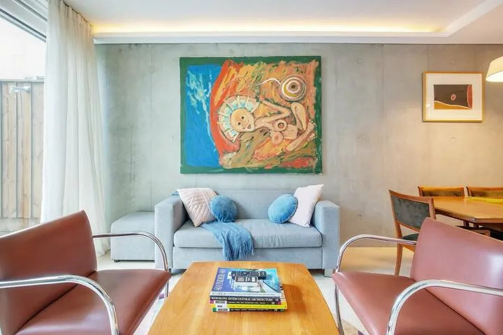 Una sala de estar con asientos alrededor de una mesa de centro de madera bajo una pintura colorida.