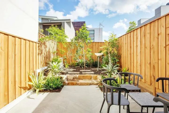 Un patio exterior pavimentado con asientos, cercas de madera y plantas.