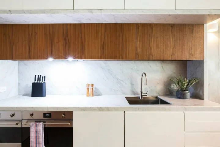 Una cocina moderna con salpicadero de mármol, fregadero y armarios superiores de madera.