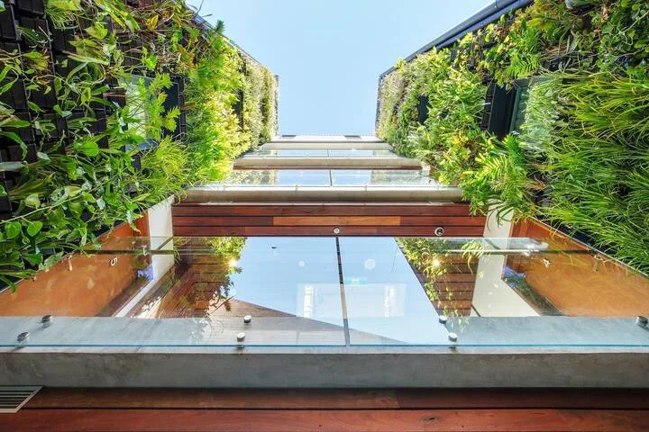 Fachada de un edificio moderno con balcones de vidrio y abundantes plantas verdes.