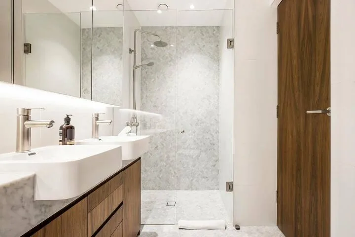 Un baño luminoso tiene un lavabo doble junto a una ducha de vidrio.