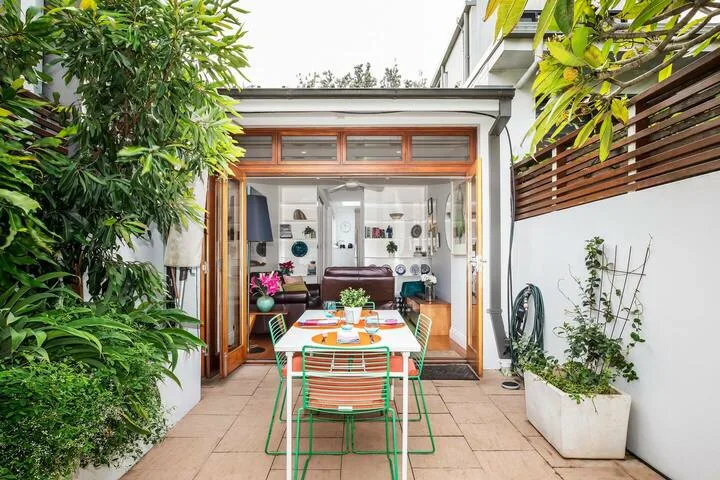 Un comedor en el patio con mesa y sillas está junto a una sala con frente de vidrio.