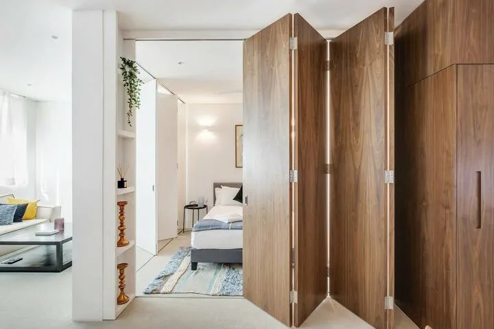 Un dormitorio luminoso con una cama y paneles de madera plegables en primer plano.