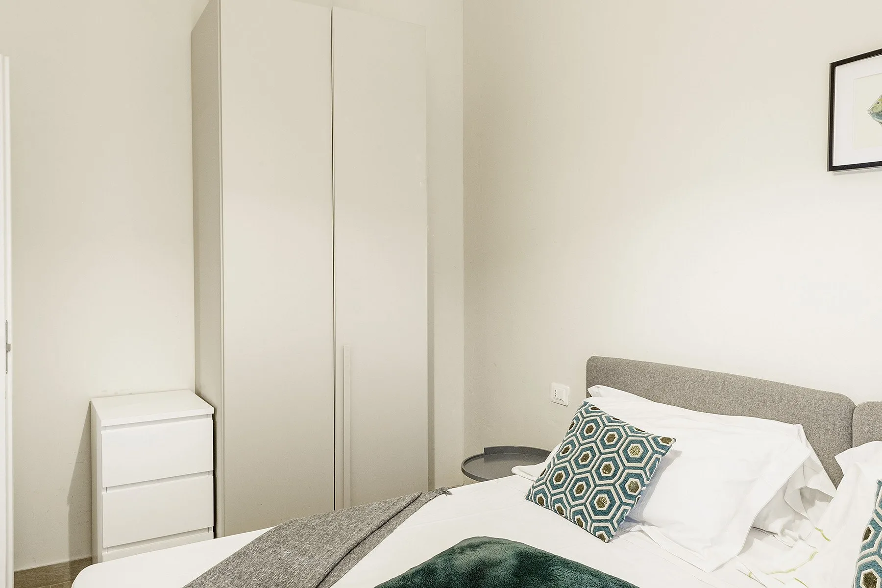 Un dormitorio con una cama tendida y un armario alto.