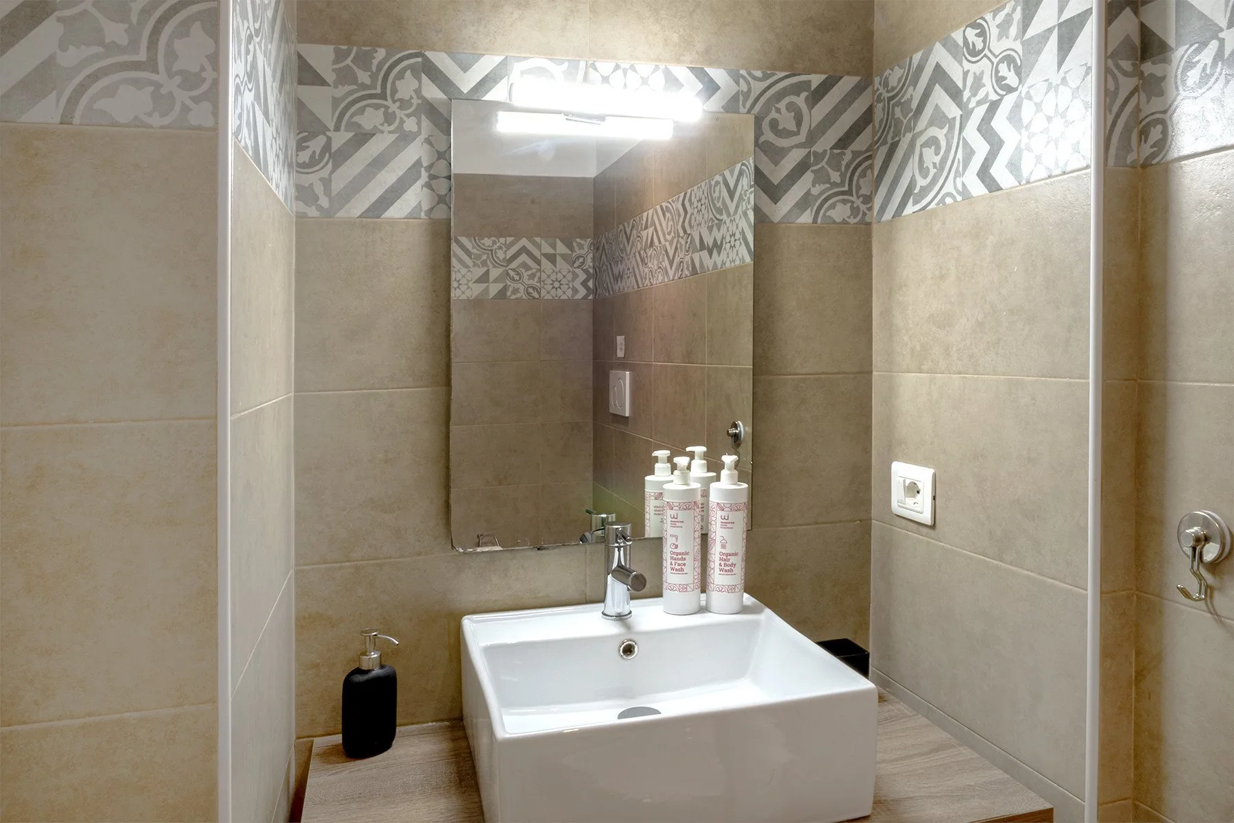 Un baño con azulejos, un lavabo blanco, un espejo y artículos de aseo.