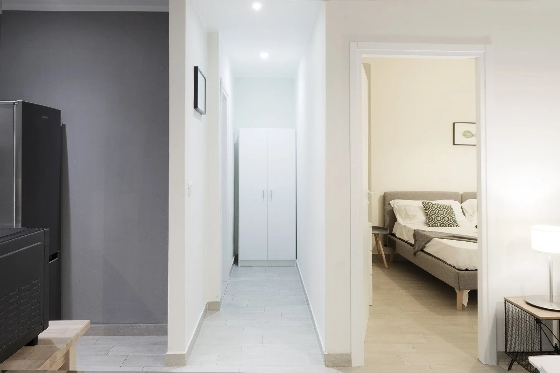 Un pasillo luminoso conduce a un dormitorio con una cama visible a través de la puerta.