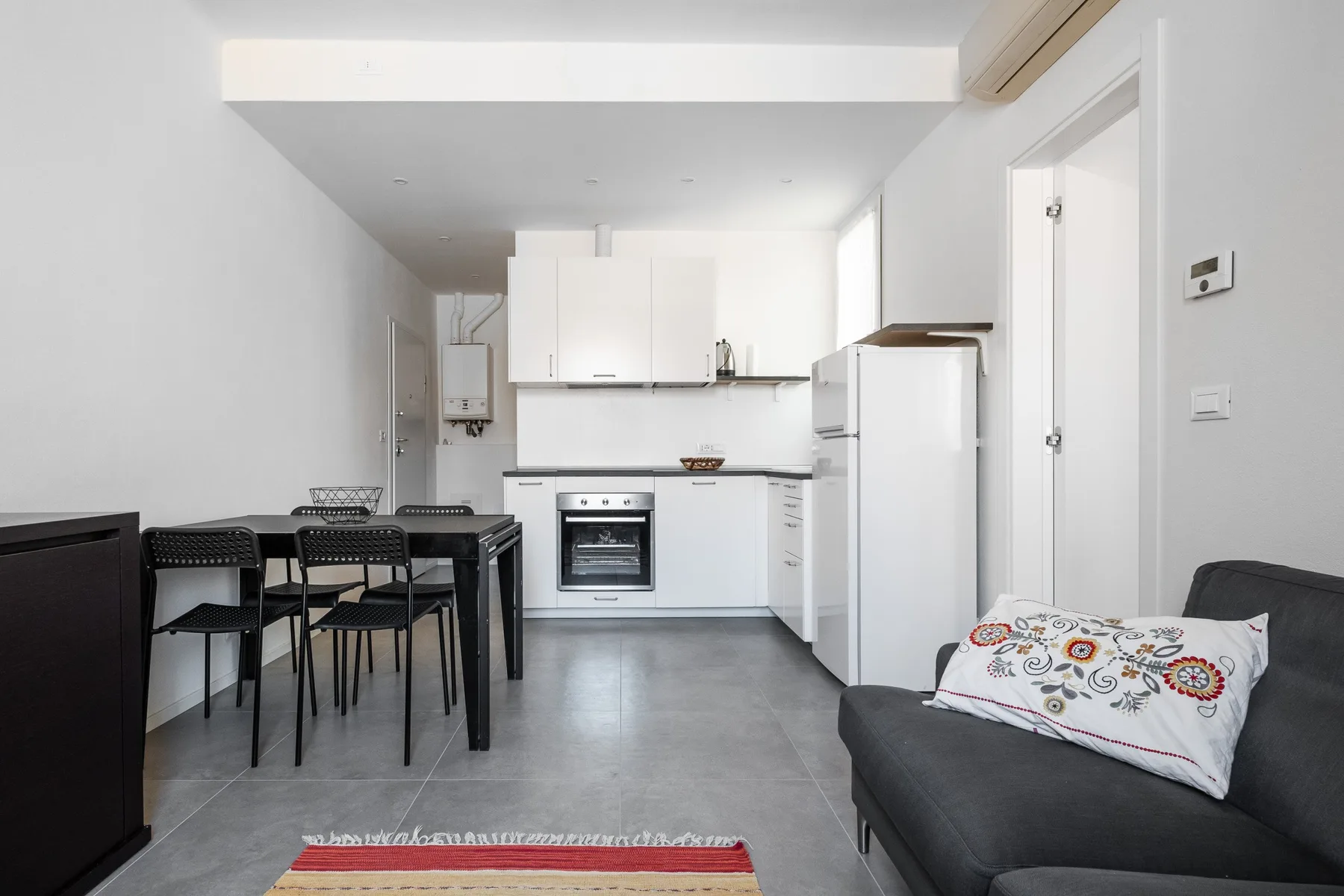 A compact kitchen and dining area opens onto a seating space with a dark sofa.