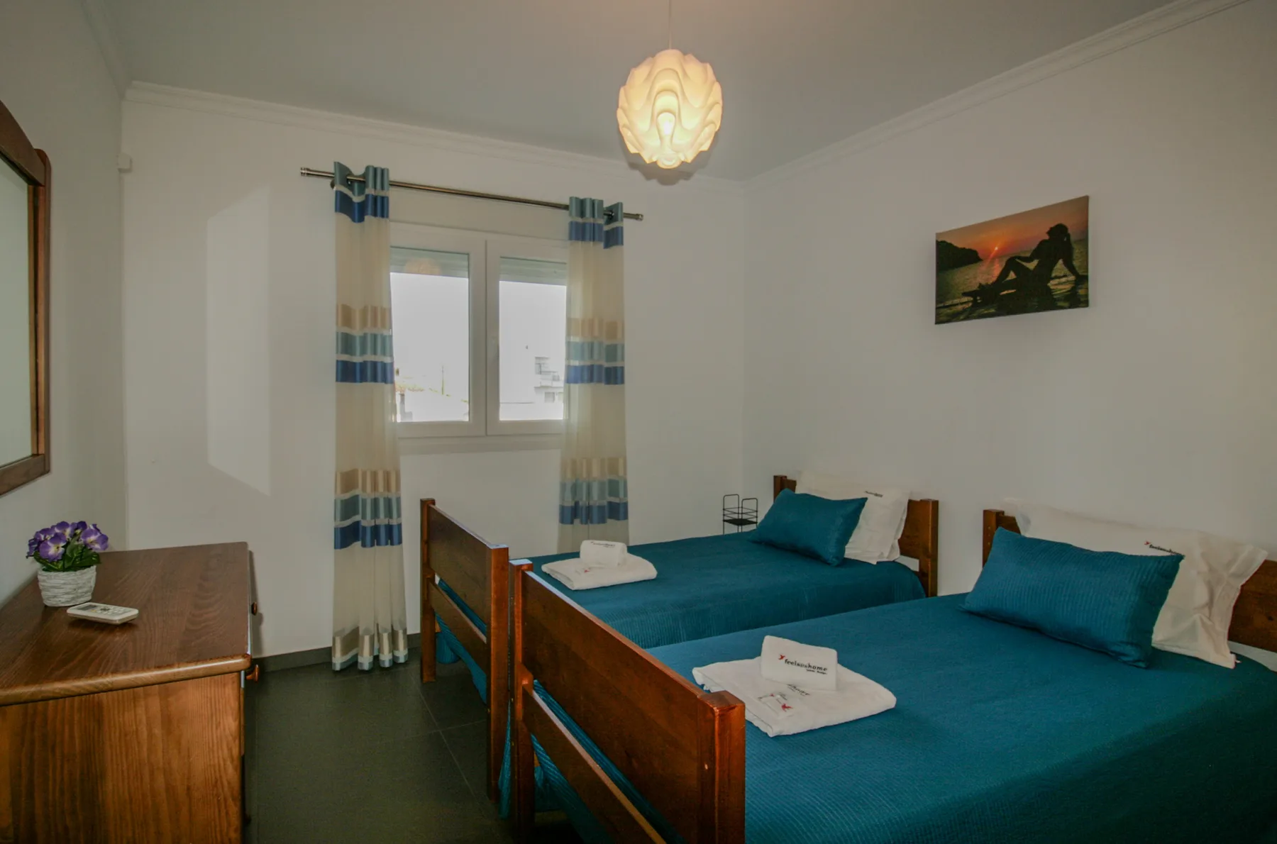 Un dormitorio con dos camas, ropa de cama verde azulado y una ventana con cortinas a rayas.