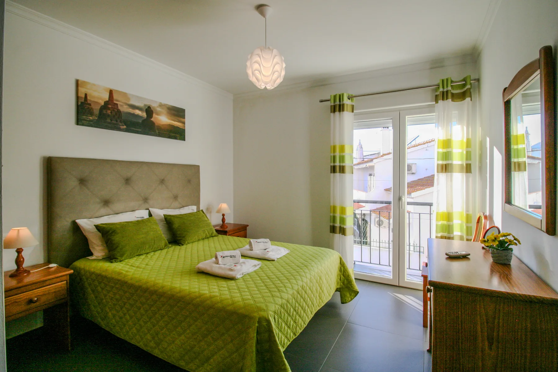 Un dormitorio con una cama vestida de verde y puertas que dan a un balcón.