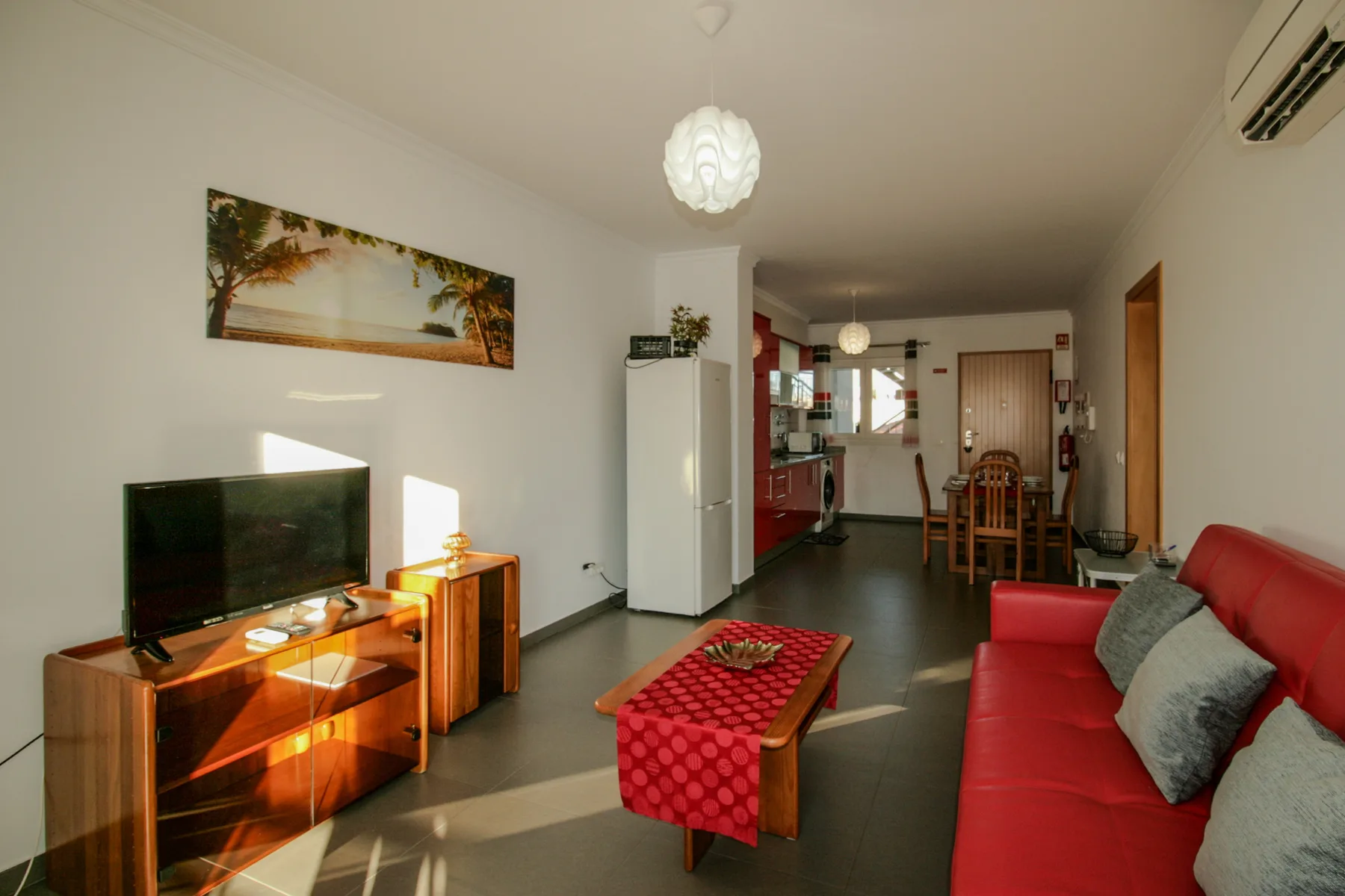 Una sala de estar con sofá rojo, televisor y comedor.