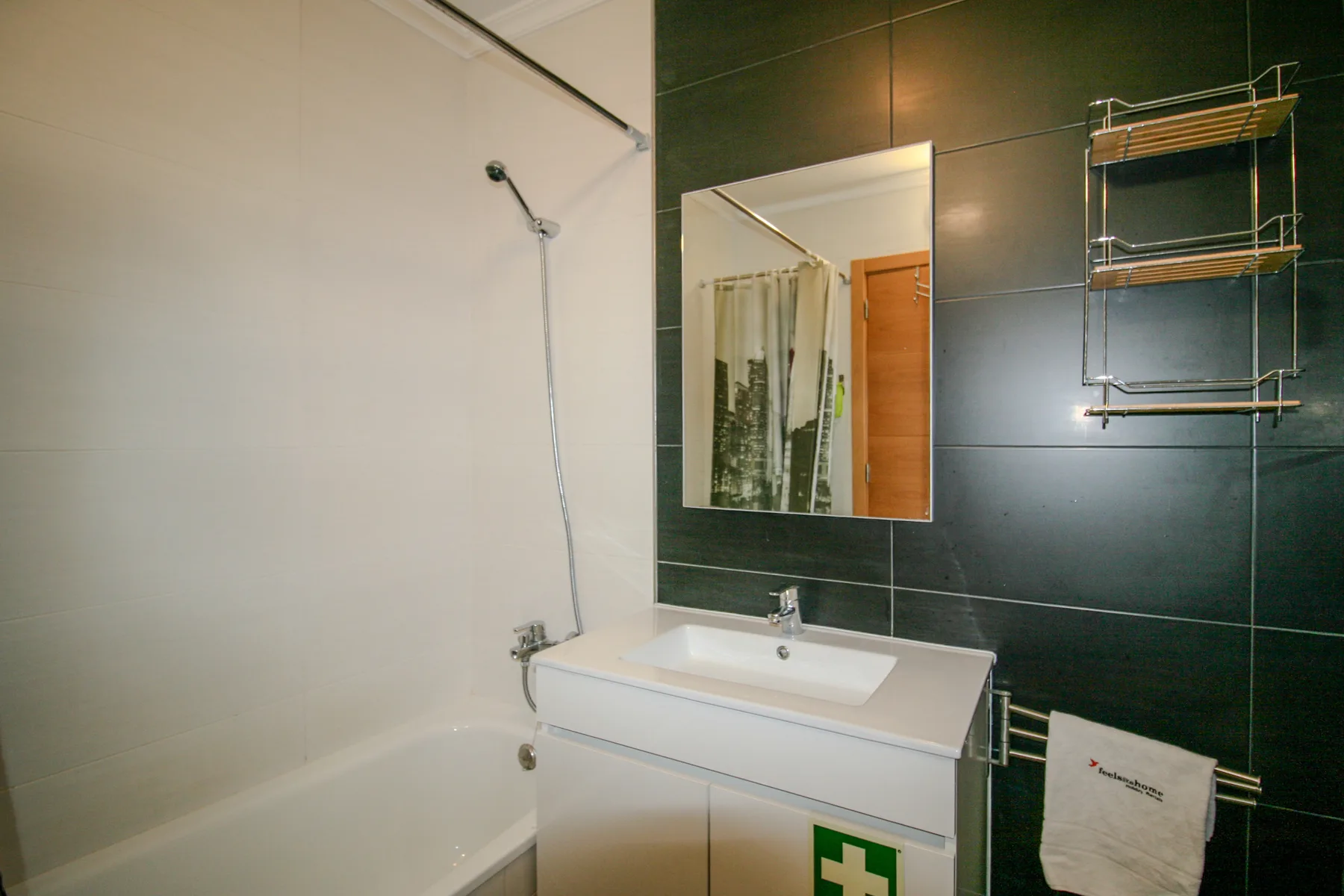 Un baño con bañera, lavabo y una pared de azulejos oscuros.