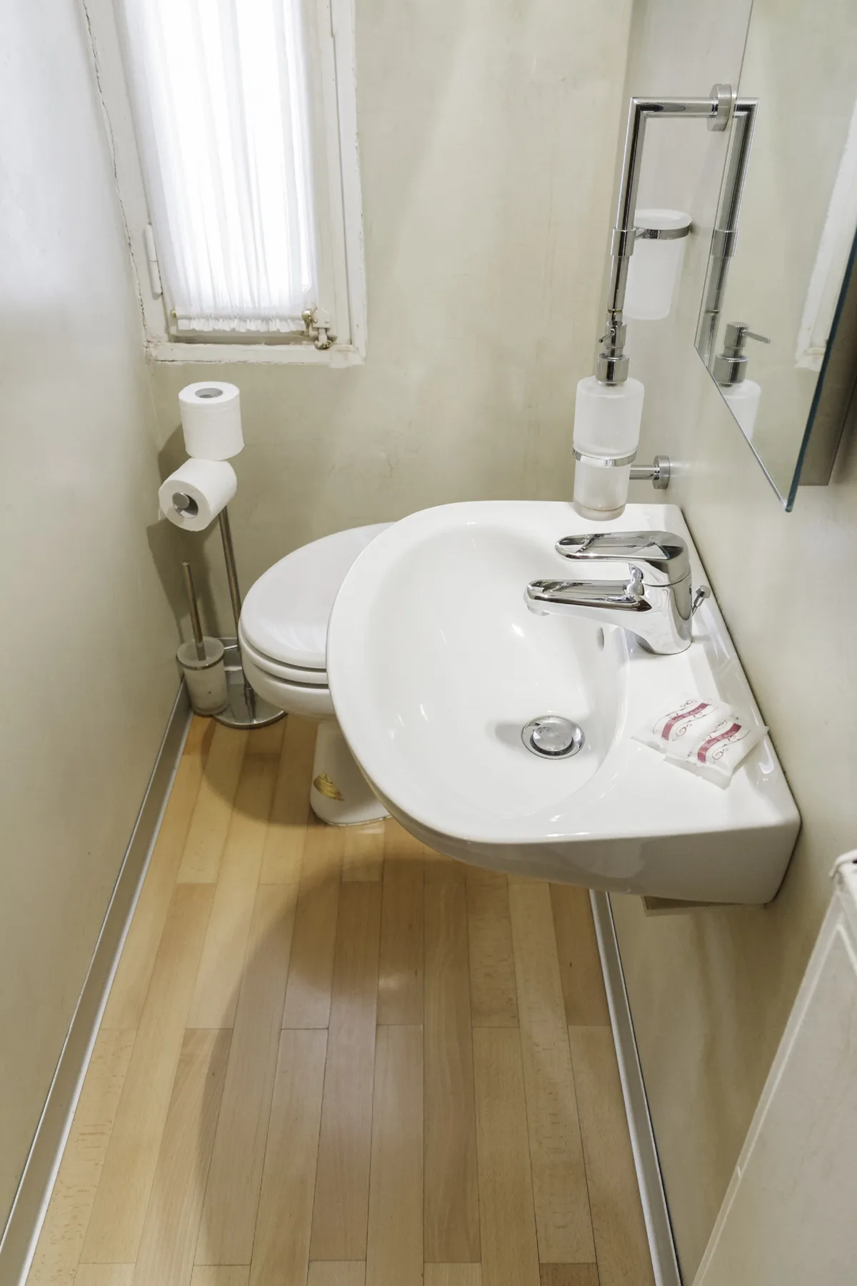 A compact bathroom with a white sink, toilet, and narrow window.