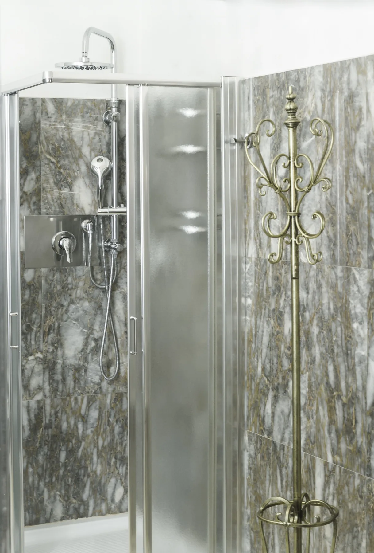 A tiled bathroom shower with a handheld showerhead and ornate metal stand.