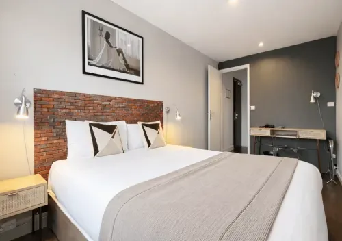 Habitación de hotel moderna con cabecero de ladrillo, ropa de cama blanca, pared de acento gris y vistas a la ciudad.